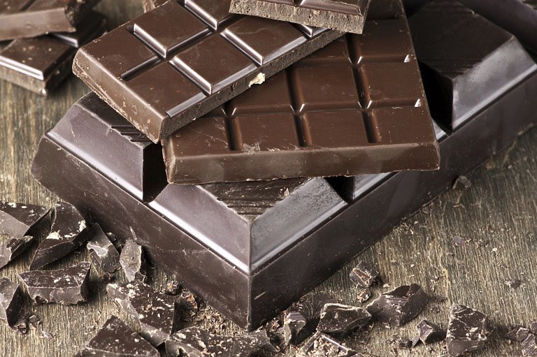 Assorted dark chocolate bars and chopped chocolate on vintage wooden background.